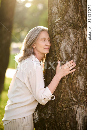 Woman with closed eyes touching tree 81437074