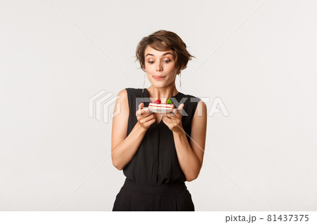 Silly beautiful girl licking lips and looking at tempting piece of cake, standing over white background 81437375
