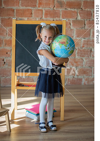 Portrait of schoolgirl standing in front of chalkboard with globe in her hands 81437810