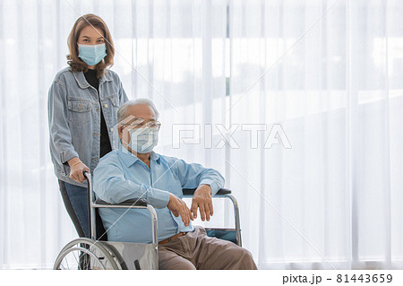 An old fat asian male patient with gray hair wearing light blue shirt and brown pants sitting on wheelchair when his daughter wearing jeans shirt stand holding the handles look at camera together An old fat asian male patient with gray hair wearing light blue shirt and brown pants sitting on wheelchair when his daughter wearing jeans shirt stand holding the handles look at camera together 81443659