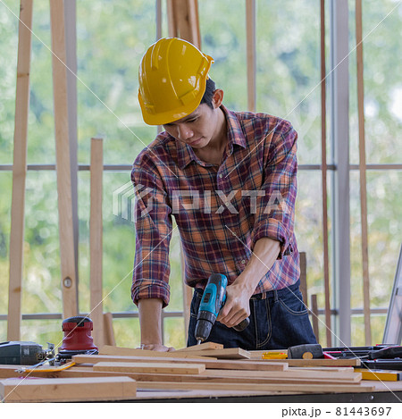 young asian handsome male wearing orange hard safty helmet lean over working table full of equipments smiling inside industrial working site 81443697