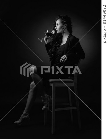 Portrait of attractive brunette with glass of wine on a black bacground. 81449032