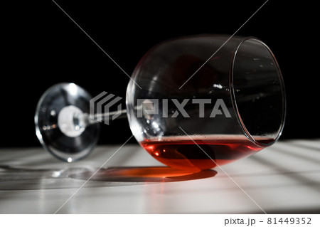 A glass of red wine lies on its side on a white table with a shade from the blinds 81449352