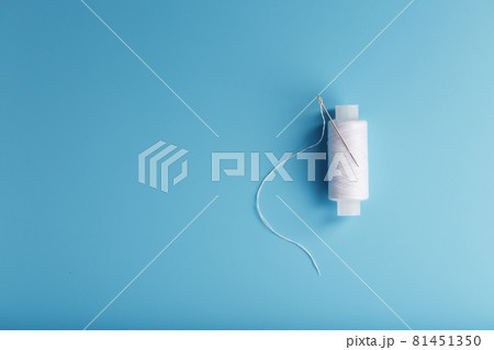 A skein of white thread with a needle on a blue background 81451350