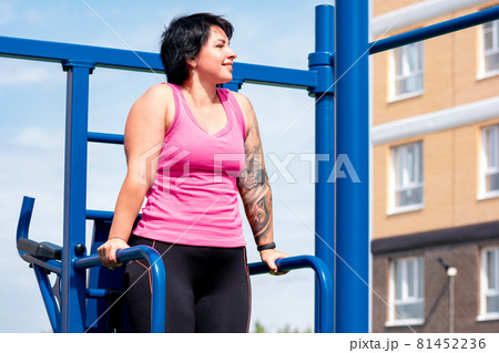 young woman performs exercises outdoors using street fitness combo machine 81452236