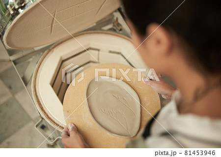 Woman putting clay plate into kiln Woman putting clay plate into kiln 81453946