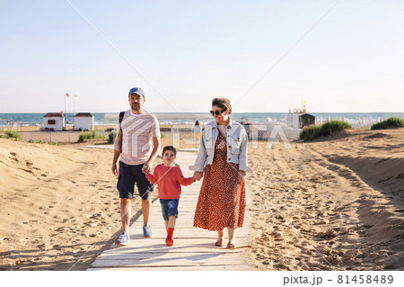 Happy family, mother father and little daughter, walking towards summer sea beach along wooden path 81458489