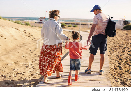 Happy family, mother father and little daughter, walking towards summer sea beach along wooden path 81458490