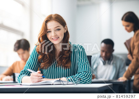 Smiling student sitting at desk in classroom posing at camera Smiling student sitting at desk in classroom posing at camera 81459297