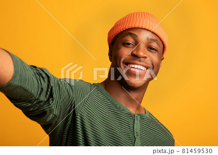Happy Young Black Guy Taking Selfie While Posing Over Yellow Studio Background Happy Young Black Guy Taking Selfie While Posing Over Yellow Studio Background 81459530