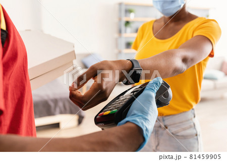 Lady Paying Deliveryman With Smartwatch For Pizza Wearing Mask Indoors Lady Paying Deliveryman With Smartwatch For Pizza Wearing Mask Indoors 81459905