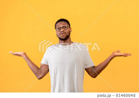Confused black guy raising hands up and looking at camera, standing over yellow studio background Confused black guy raising hands up and looking at camera, standing over yellow studio background 81460048