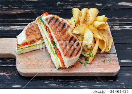 Grilled veggie sandwich with vegetables and herbs, cut in half on a wooden kitchen board. Garnish with potatoes. Close-up. 81461455