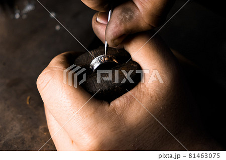 Close-up of hand of a goldsmith setting the diamond on the ring. Craft jewelery making with professional tools.  81463075
