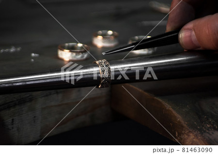 Close-up of hand of a goldsmith setting the diamond on the ring. Craft jewelery making with professional tools.  81463090