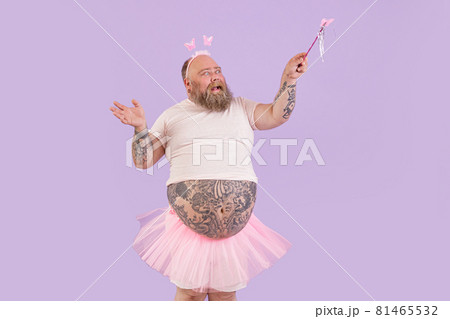 Expressive man with overweight in fairy suit waves magic stick on purple background 81465532