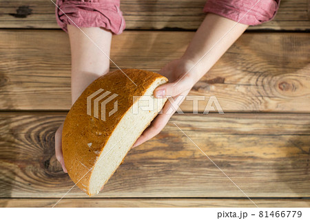 Women's hands hold half of a round wheat bread over a wooden counter. 81466779