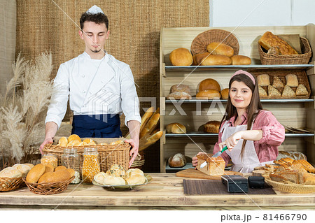 The saleswoman starts cutting the bread and the baker arranges the rolls and other goods in the store. Family bakery and shop. The saleswoman starts cutting the bread and the baker arranges the rolls and other goods in the store. Family bakery and shop. 81466790