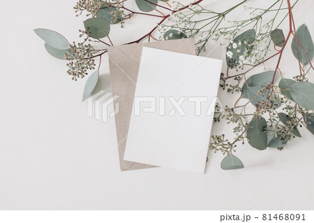 Wedding, birthday stationery composition. Blank greeting card, invitation mockup and craft envelope. Green Eucalyptus populus branches, Gypsophila flowers isolated on table background. Flat lay, top. 81468091