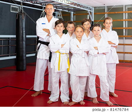 Portrait of group of children in white kimono with trainer in gym 81476784