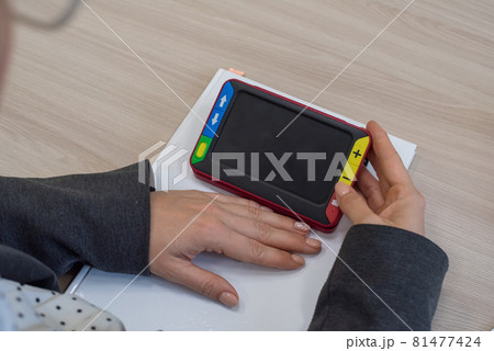 The woman is holding a reading device for the visually impaired. Electronic magnifier for the nearsighted 81477424