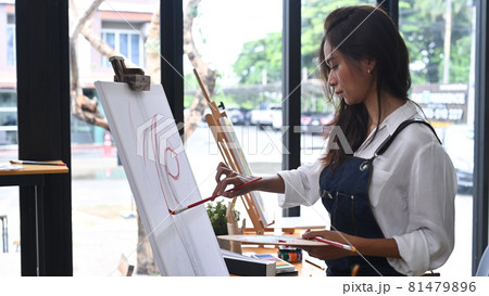 Side view female artist painting with watercolor on easel in art studio. Side view female artist painting with watercolor on easel in art studio. 81479896