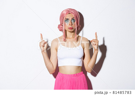 Portrait of miserable cute party girl in pink wig, sobbing and pouting upset, looking disappointed and pointing fingers up, standing over white background Portrait of miserable cute party girl in pink wig, sobbing and pouting upset, looking disappointed and pointing fingers up, standing over white background 81485783