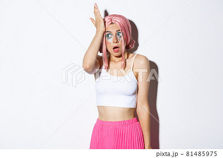 Portrait of silly forgetful girl slap her forehead and gasping, remember something, standing in halloween costume with bright makeup and pink wig 81485975