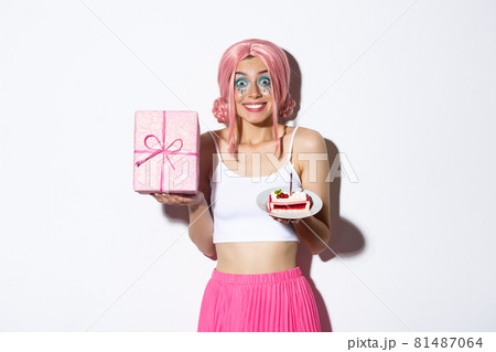 Portrait of excited birthday girl celebrating her holiday, holding b-day gift and cake, smiling happy, standing over white background Portrait of excited birthday girl celebrating her holiday, holding b-day gift and cake, smiling happy, standing over white background 81487064