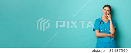 Coronavirus, pandemic and social distancing concept. Image of pleased and thoughtful female doctor in scrubs, looking at upper left corner and thinking, smiling intrigued 81487549