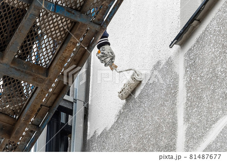 A industrial worker on a lifting platform paints the facade of a new modern urban building under construction at a construction site 81487677