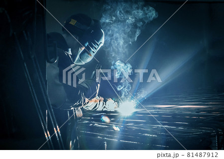 A masked working man is doing welding work on metal structures in a factory or industrial enterprise 81487912