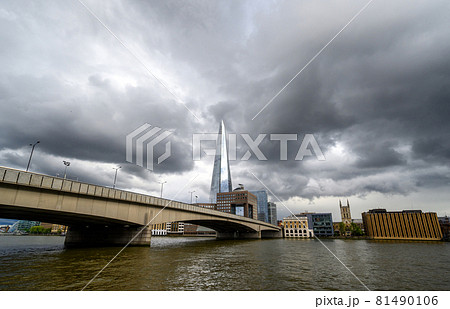 London, UK: View from the City of London looking south across the River Thames with London Bridge and the Shard building. Light reflecting on The Shard with dark storm clouds behind. 81490106