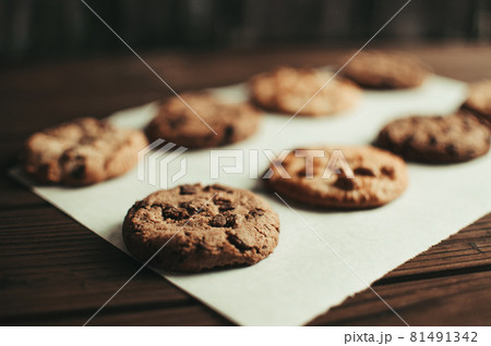 Chocolate covered cookies lay on a parchment paper in a row. Gluten-free cookies on a wooden table out of the oven. Selective focus Chocolate covered cookies lay on a parchment paper in a row. Gluten-free cookies on a wooden table out of the oven. Selective focus 81491342