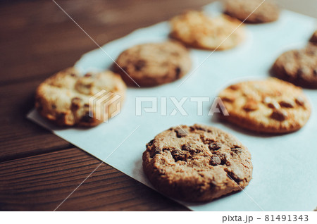 Chocolate covered cookies lay on a parchment paper in a row. Gluten-free cookies on a wooden table out of the oven. Selective focus Chocolate covered cookies lay on a parchment paper in a row. Gluten-free cookies on a wooden table out of the oven. Selective focus 81491343