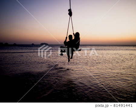 Silhouettes of children's rope swings at the golden hour sunset sea background 81491441