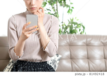 携帯電話（スマートフォン）を持ちながら悩む若い黒髪の女性 81492418