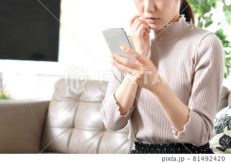 携帯電話（スマートフォン）を持ちながら悩む若い黒髪の女性 81492420