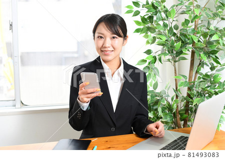 スーツを着た黒髪の若い女性がスマホ・スマートフォン（携帯電話）を見るイメージ 81493083