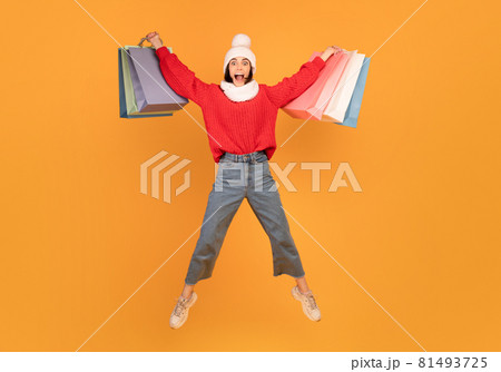 Big sales concept. Joyful shopaholic lady jumping with shopping bags, wearing knitted hat and winter jacket 81493725