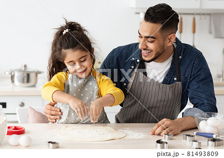 Cheerful arab dad and little daughter baking together in kitchen, making pizza 81493809