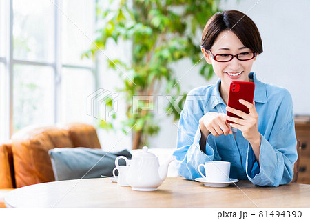 リビングで紅茶を飲みながらスマホを使う眼鏡のミドル女性 81494390