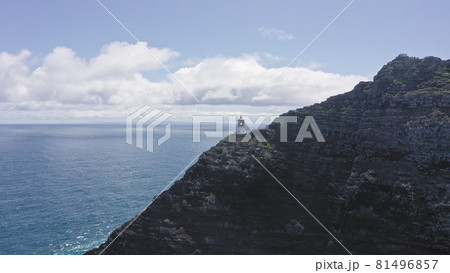 Flying drone over the ocean. View of makapuu lighthouse. Waves of Pacific Ocean wash Rocky shore. Magnificent mountains of Hawaiian island of Oahu against backdrop of blue sky with white clouds. Flying drone over the ocean. View of makapuu lighthouse. Waves of Pacific Ocean wash Rocky shore. Magnificent mountains of Hawaiian island of Oahu against backdrop of blue sky with white clouds. 81496857