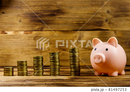 Pink piggy bank and stacks of coins on wooden background. Saving money concept Pink piggy bank and stacks of coins on wooden background. Saving money concept 81497253