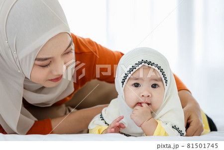 A cute and beautiful Asian Muslim in hijab dress playing with her daughter on bed A cute and beautiful Asian Muslim in hijab dress playing with her daughter on bed 81501745