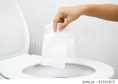 close up hand holding a tissue to be thrown into the toilet bowl. Can not drain water of toilet paper in cause the stool to clog up. WC 81501815