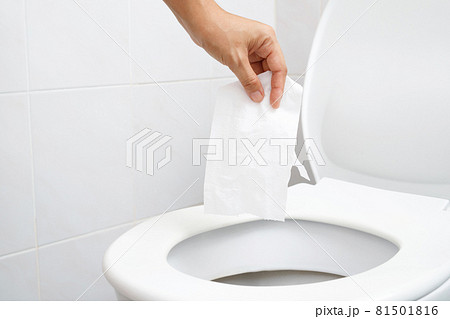 close up hand holding a tissue to be thrown into the toilet bowl. Can not drain water of toilet paper in cause the stool to clog up. WC 81501816