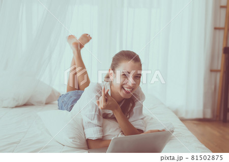 Happy woman shopping online and using laptop in bedroom 81502875