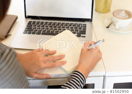 Closeup, Female accountant taking notes on notebook with opened laptop on desk 81502950