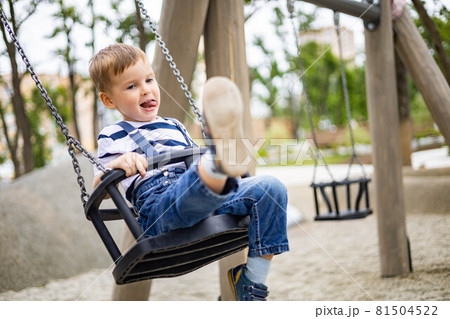 Smiling boy riding on swing at amusement forest park or childish playground having positive emotion Smiling boy riding on swing at amusement forest park or childish playground having positive emotion 81504522